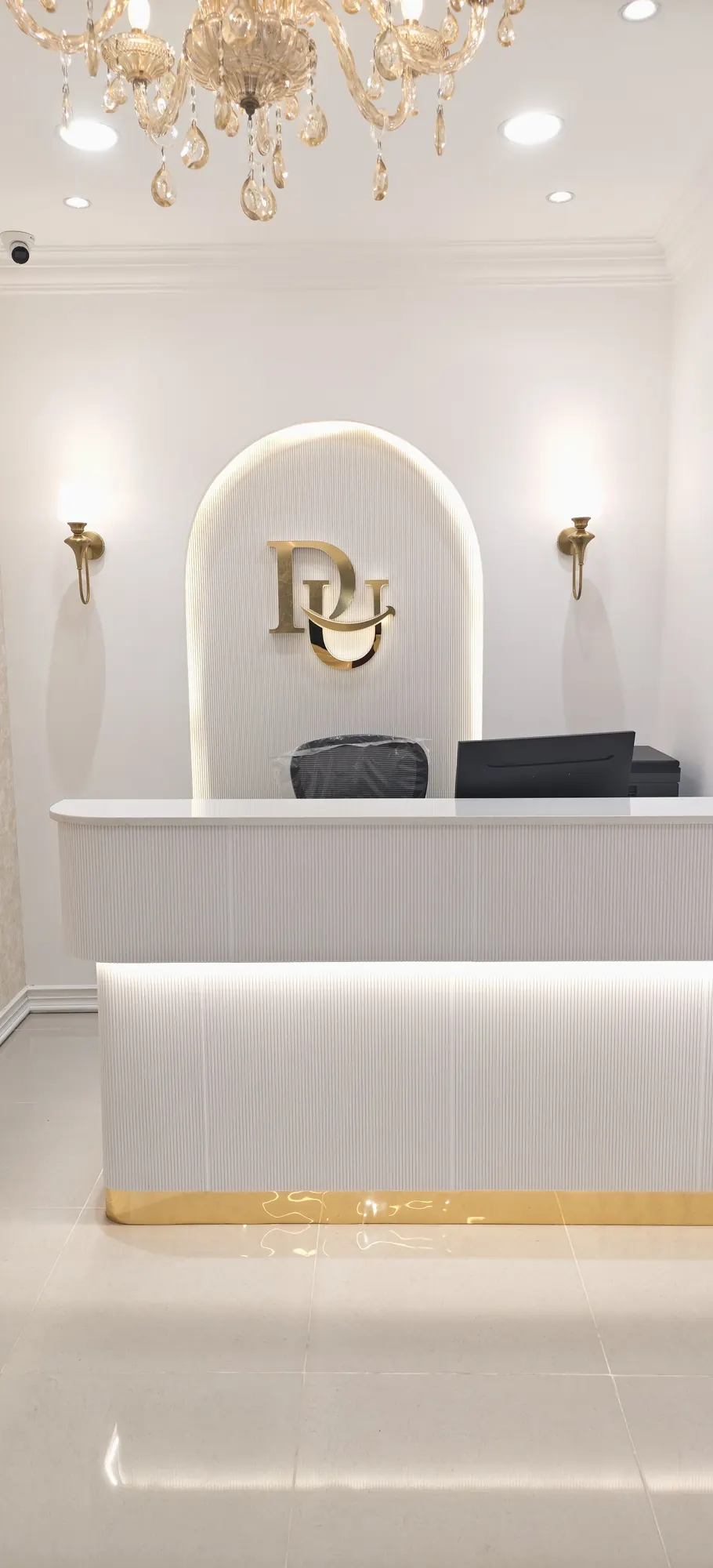 The gold monogram in a lit arched niche above the reception desk, under a crystal chandelier