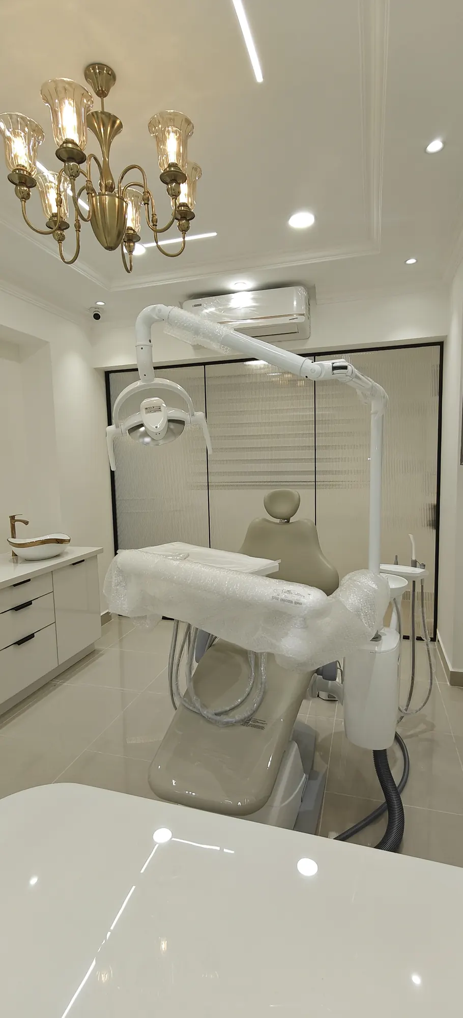A dental chair beneath a crystal chandelier in a white treatment room